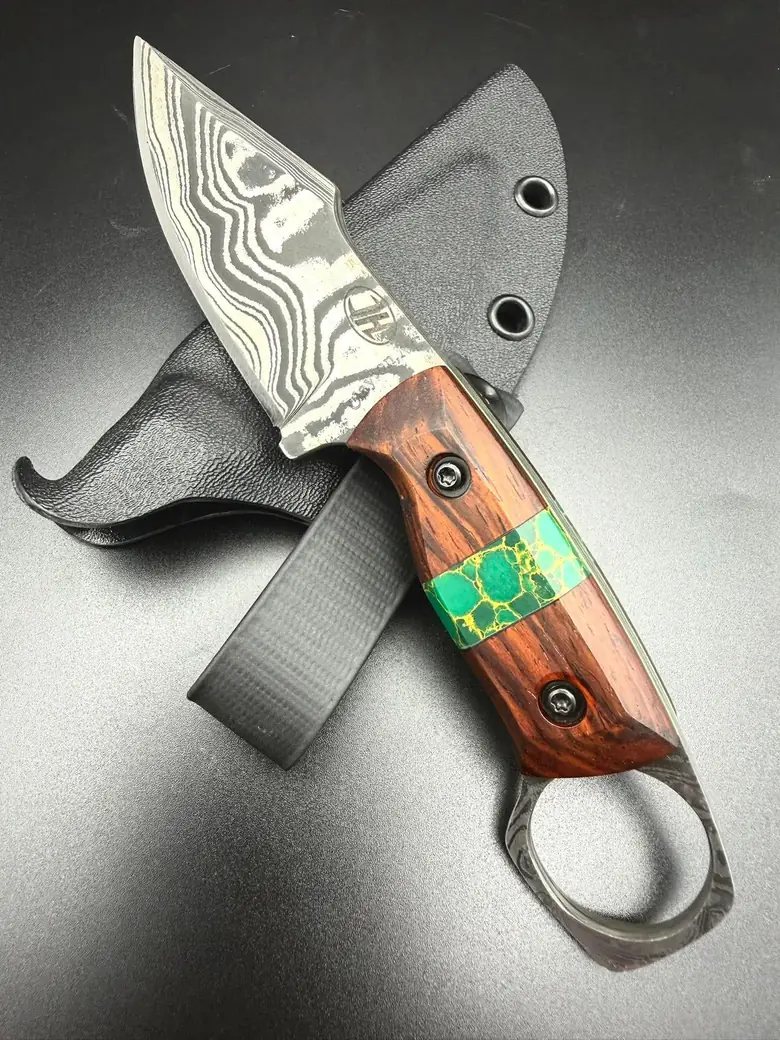 A Josh Henry Damascus finger-ring knife with a turquoise inlay in a red-brown handle, laid on its Kydex sheath